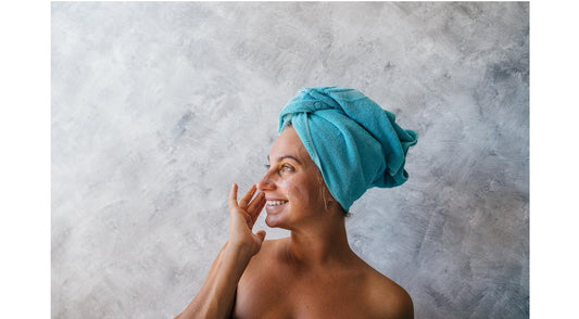 Woman with towel wrapped on head applying organic skincare products on her face